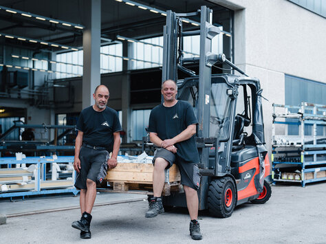 Zwei Mitarbeiter im Lager von Glasbau Wiedemann. Sie sitzen auf den Zinken eines Gabelstaplers.